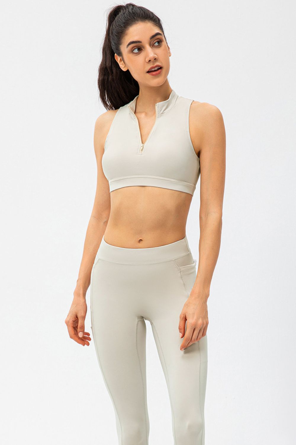 High-neck zip-front active crop top in light beige with a gold zipper detail.
