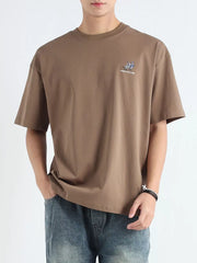 Men's relaxed fit graphic tee in Desert Color cotton with a small chest graphic and text.