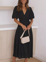 Black midi dress with V-neck, puff sleeves, and smocked waist, styled with a cream crossbody bag.