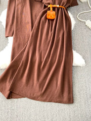 Brown knitted maxi dress and cardigan ensemble with orange belt and mini bag detail.
