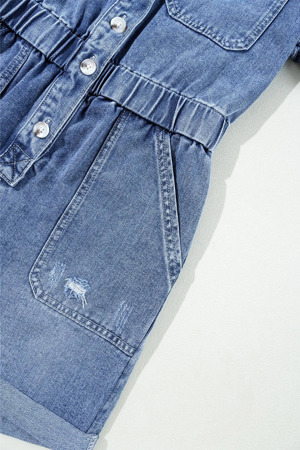 Medium wash denim romper with elastic waist, button-down front, and distressed pocket detail.