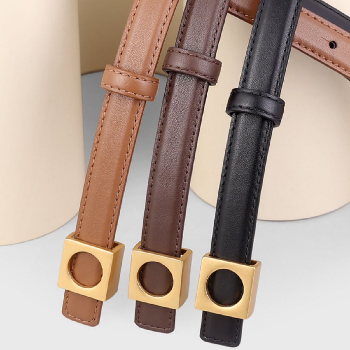 Skinny cowhide leather belts in brown, olive brown, and black with gold square buckles.