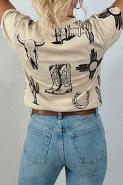 Cream crew neck t-shirt with western graphic print including bull skull, boots, cactus, horseshoe and sun symbol.