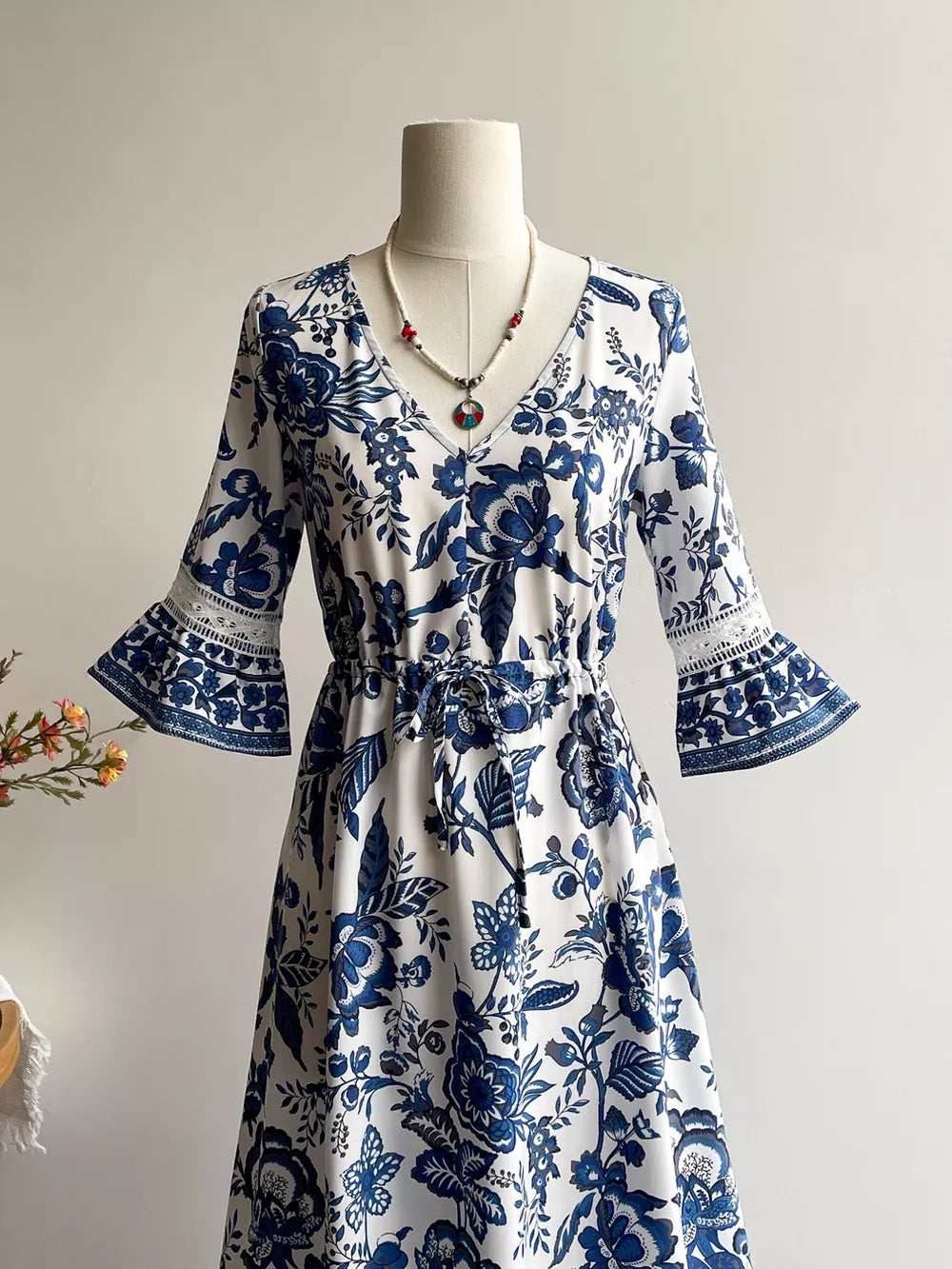Maxi dress with blue floral print, V-neck, drawstring waist, and lace-trimmed bell sleeves.
