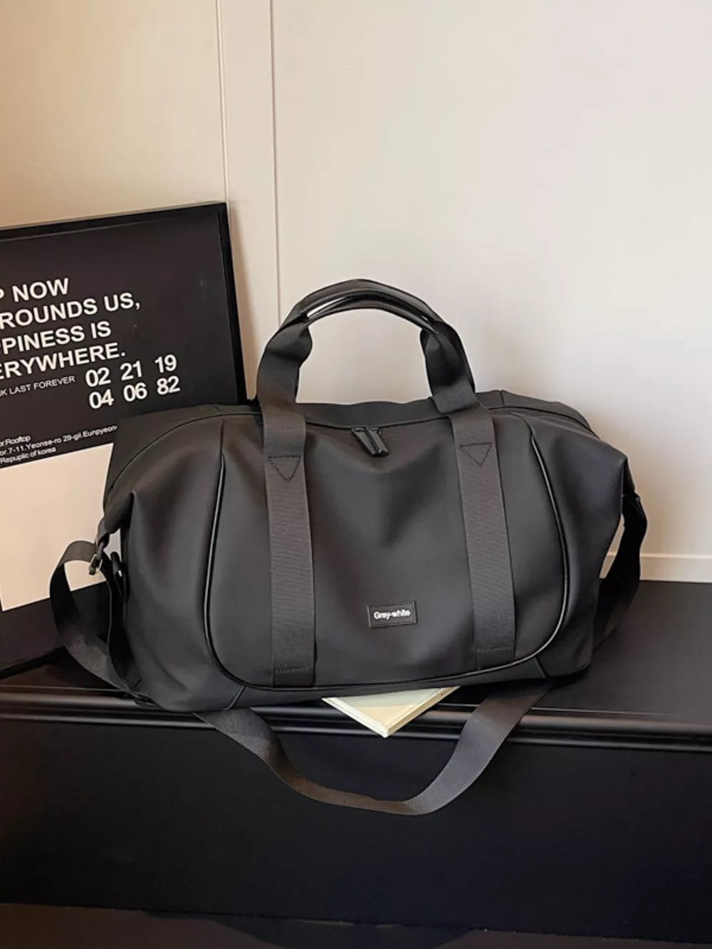 Black nylon travel duffle bag with adjustable strap and curved stitching detail.