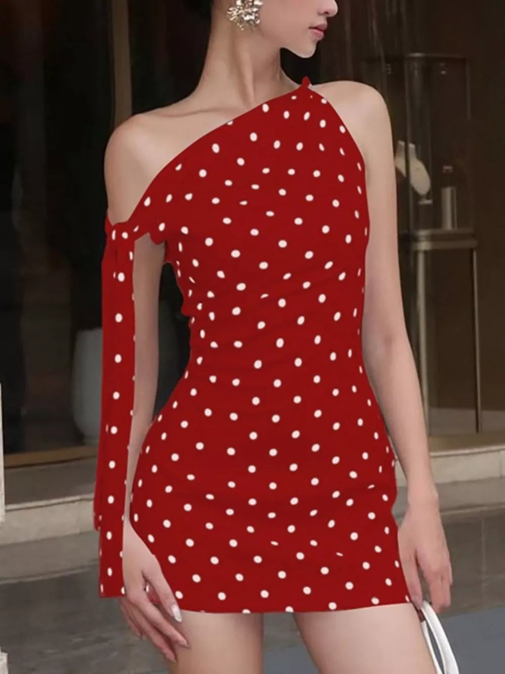 Red polka dot mini dress with asymmetrical neckline and single cold shoulder sleeve with bow detail.