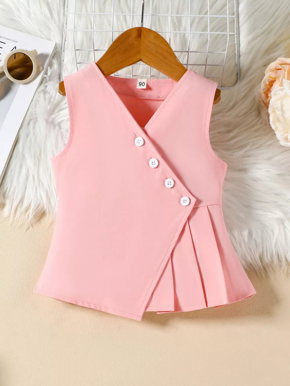 Pink baby girls sleeveless top with V-neck, asymmetrical buttons, and pleated hem.