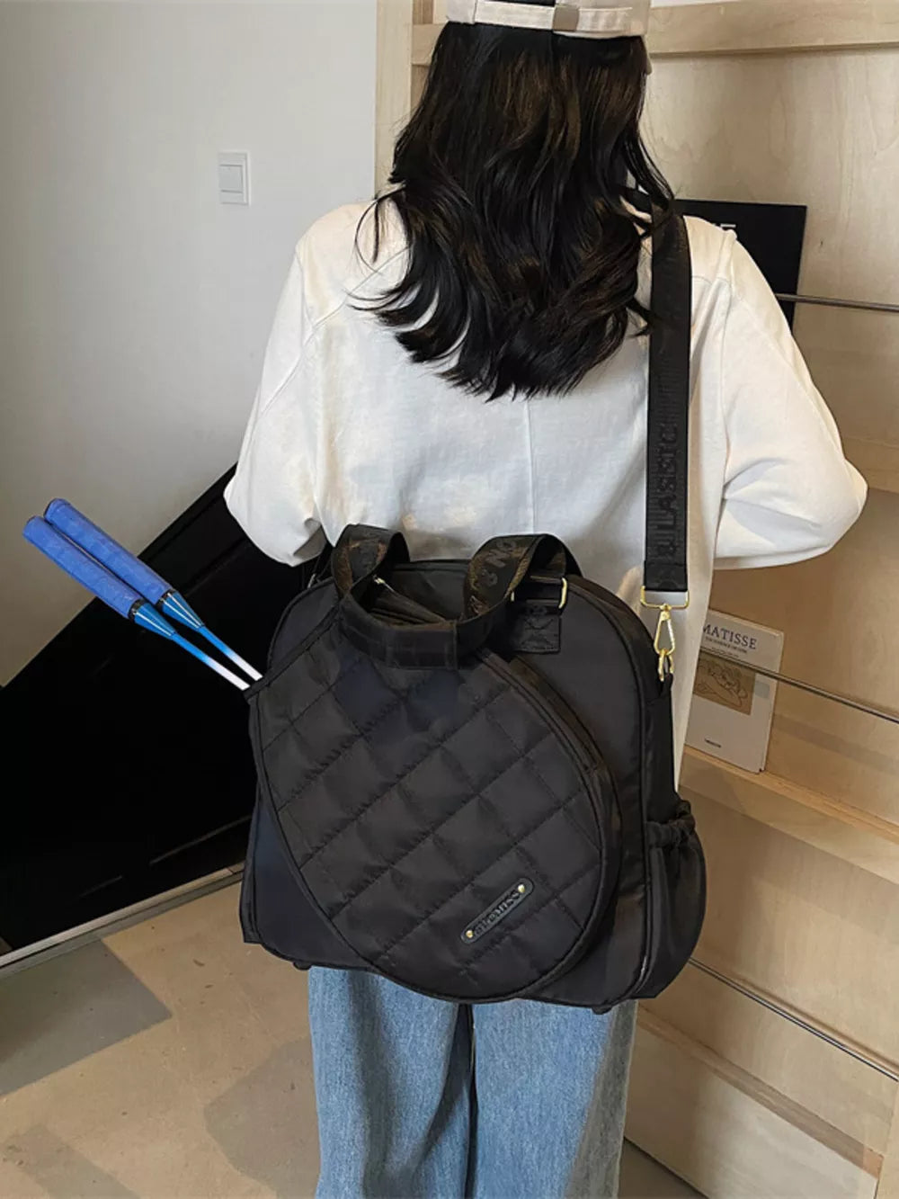 Black quilted Oxford bag for racket storage with adjustable strap and side pockets.