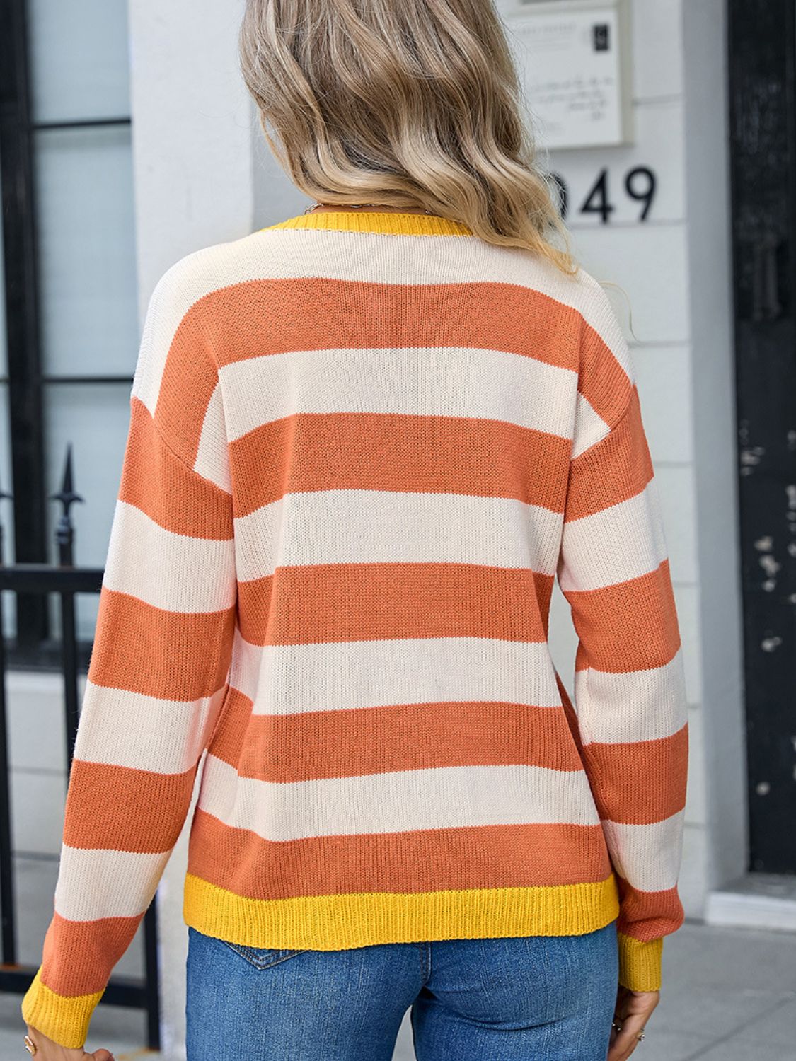 Striped acrylic sweater with ribbed cuffs and hem in orange and cream, yellow neckline.