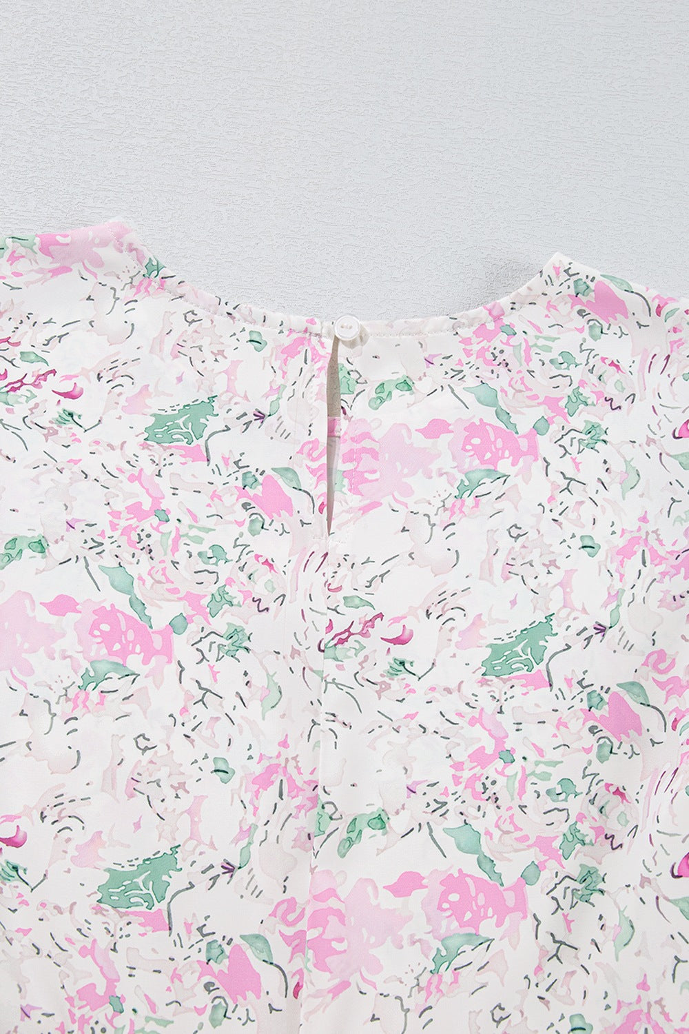 Blush pink floral print blouse with smocked waist detail and button closure at back neck.