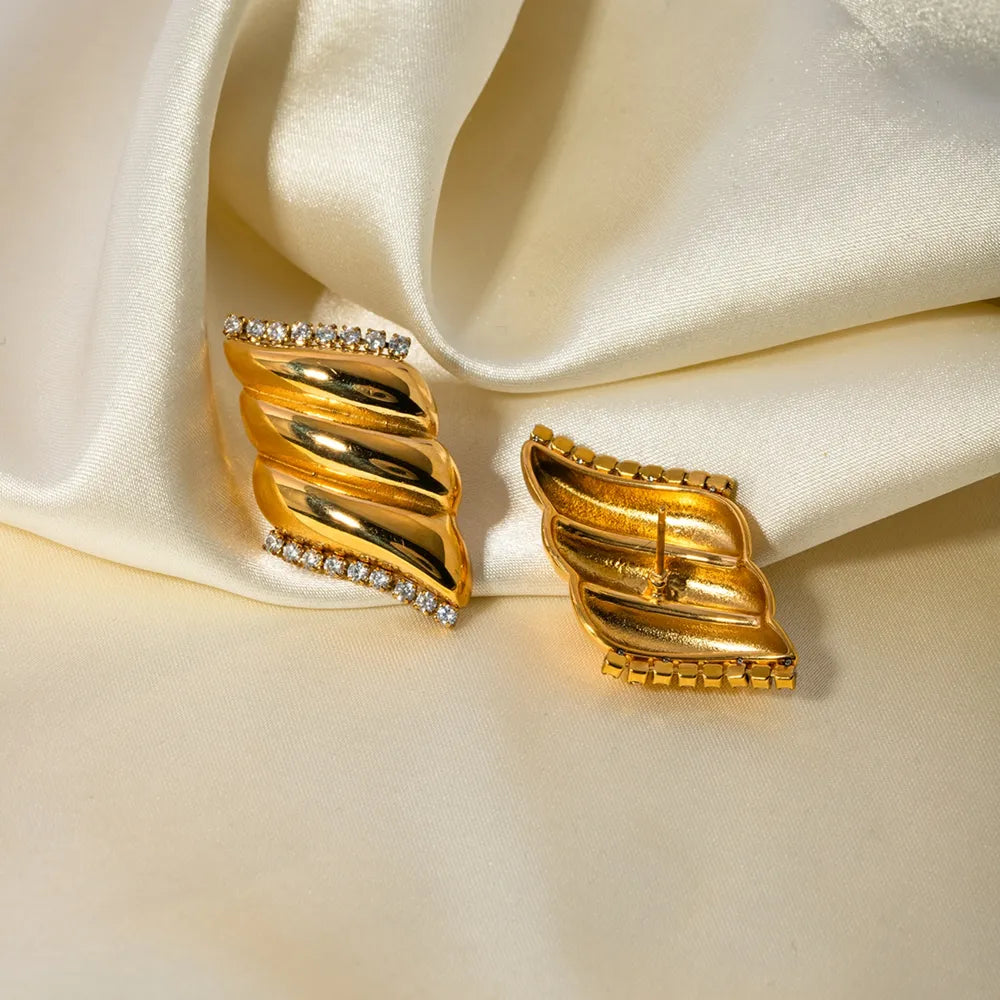 Sculptural wave crystal stud earrings in gold with 18K gold plating and sparkling crystals.