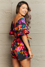 Off-shoulder playsuit with abstract print, ruffle sleeves, and multicolor pattern.