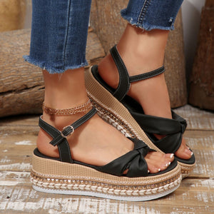Black bow knot wedge sandals with ankle buckle, braided trim, and stud detail.