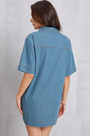 Denim mini dress in medium wash with short sleeves, collared neckline, and visible pocket detail.