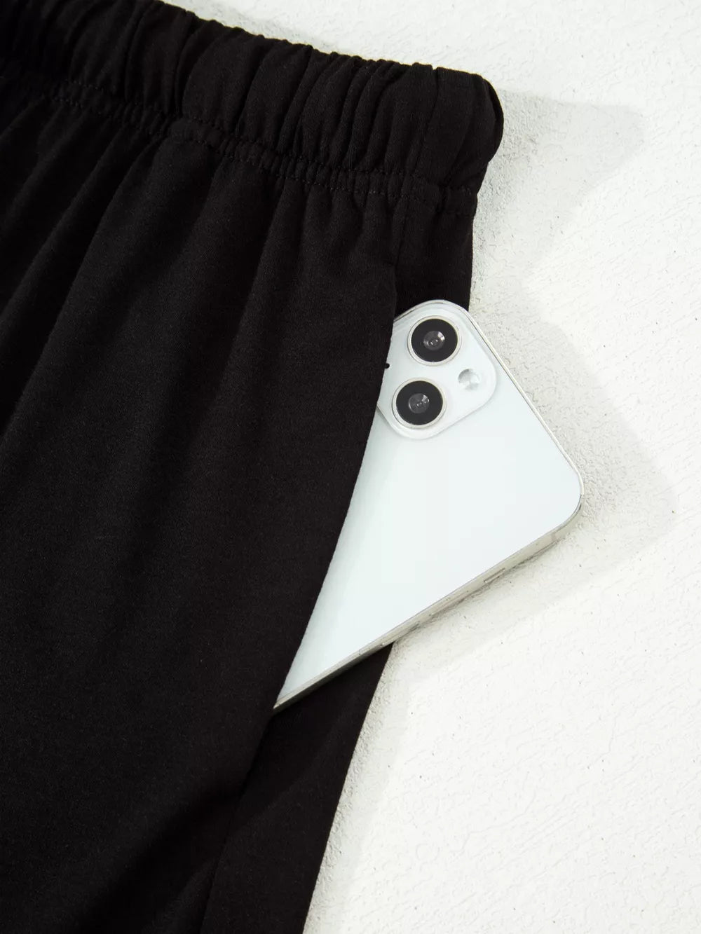 Black pajama pants with elastic waist and side pocket holding a smartphone.