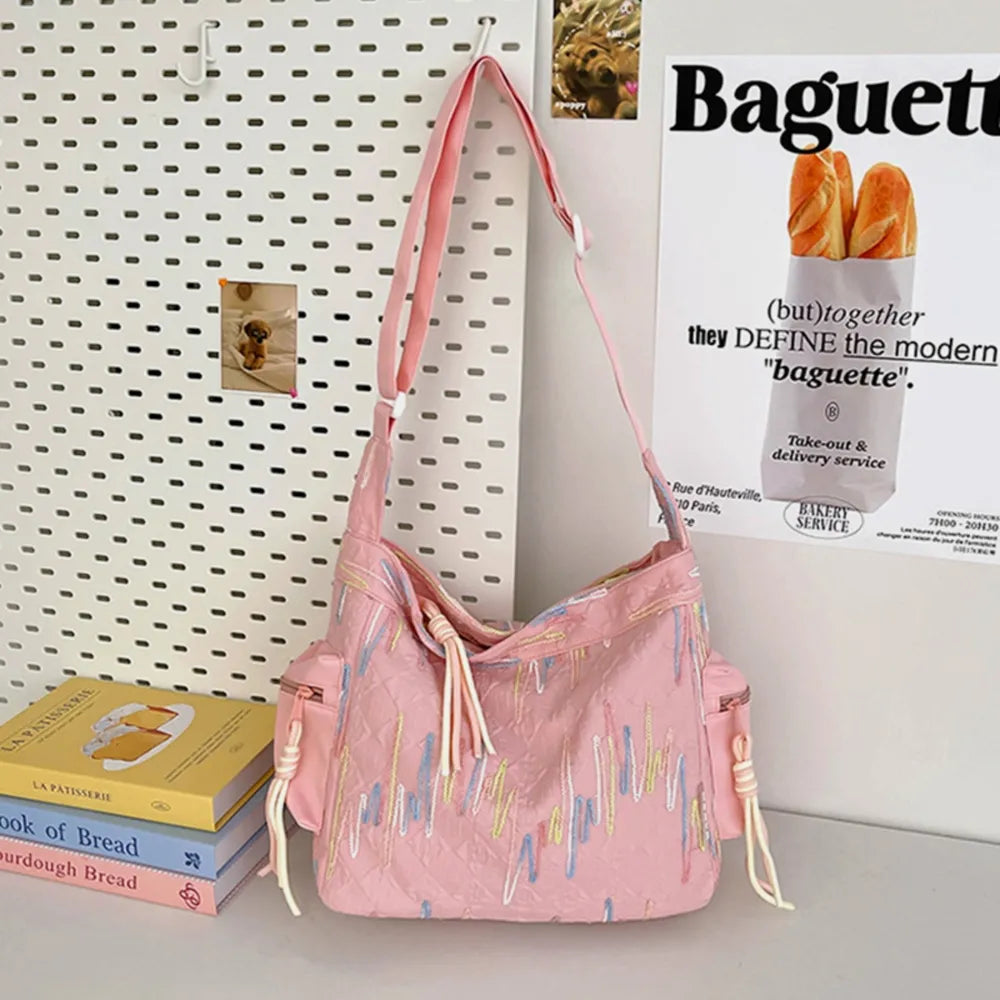 Pink slouchy shoulder bag with embroidered wavy lines and tassel details.