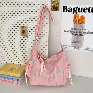 Pink slouchy shoulder bag with embroidered wavy lines and tassel details.