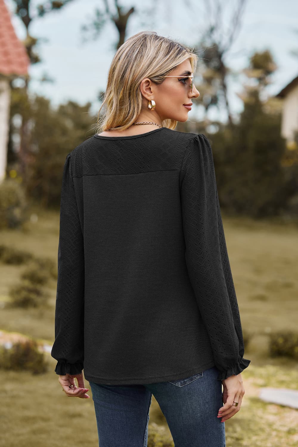 Black waffle knit blouse with perforated details and ruffled cuffs.