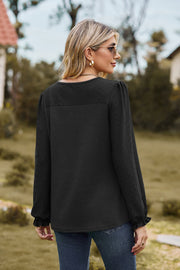 Black waffle knit blouse with perforated details and ruffled cuffs.