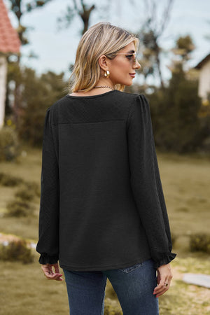 Black waffle knit blouse with perforated details and ruffled cuffs.