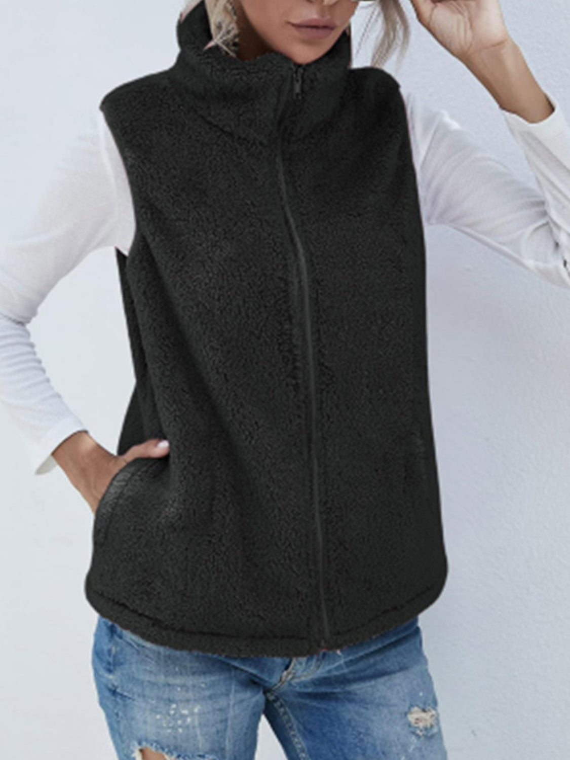 Black teddy fleece stand-collar vest with zipper and pockets, worn over a white long-sleeve shirt.