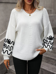 White voluminous knit sweater with black embroidered wavy sleeves and V-neck.