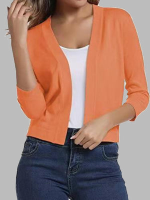 Cropped orange knit cardigan with elbow sleeves and open front, worn over a white top.