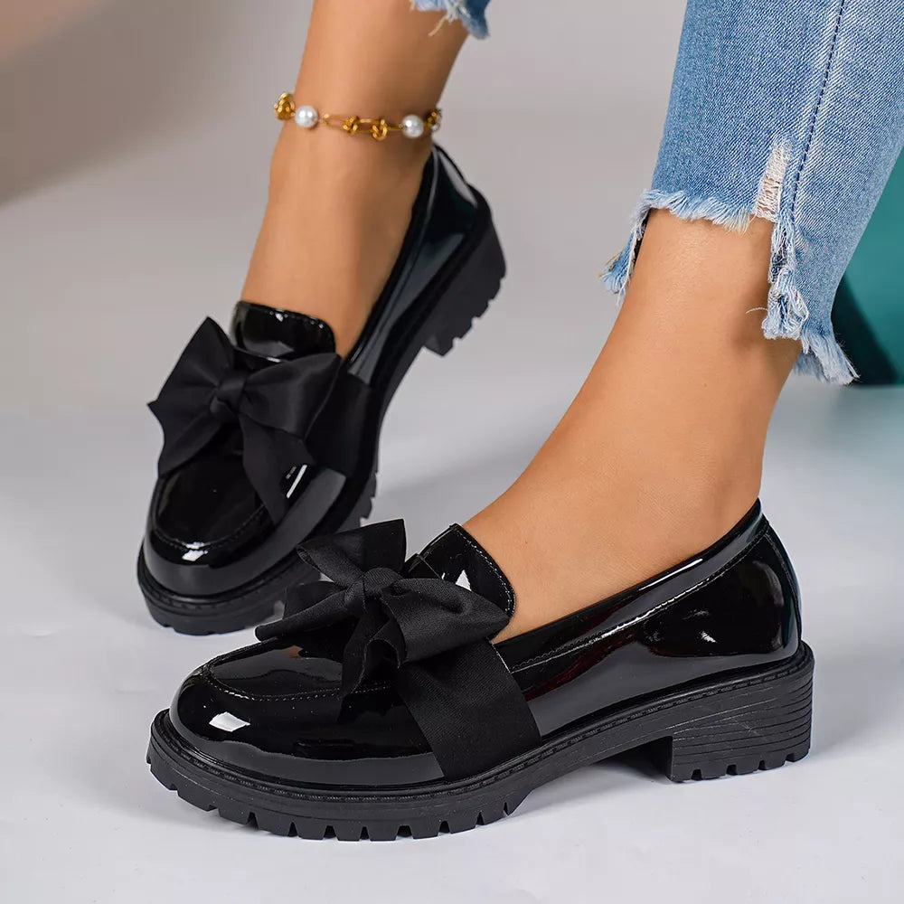 Black patent loafers with large bow detail and lug sole.