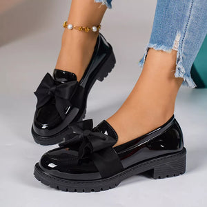Black patent loafers with large bow detail and lug sole.