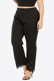 Black flare trousers with floral cutout hemline detail and elastic waistband.