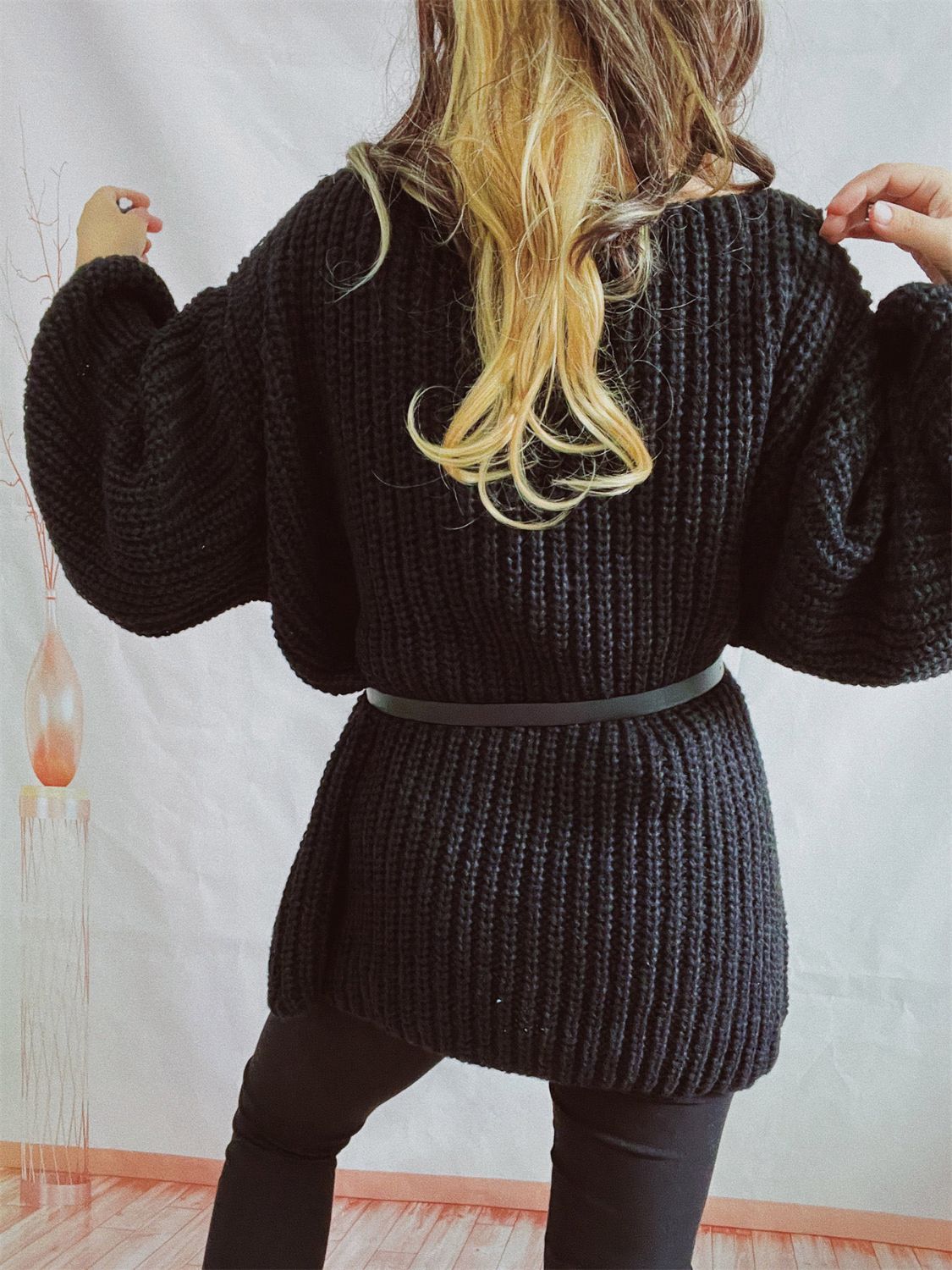 Black oversized ribbed knit sweater with belted waist and balloon sleeves.