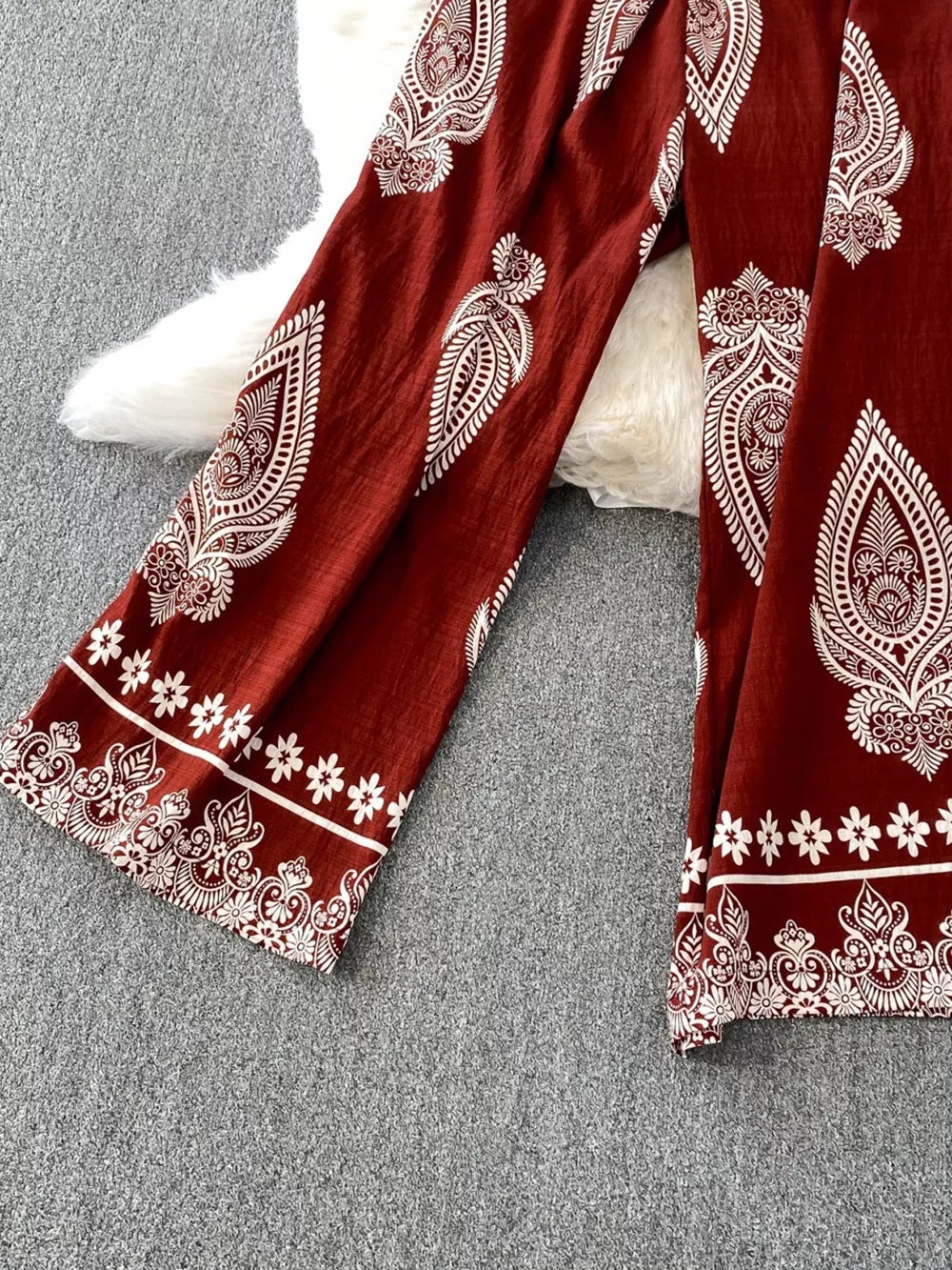 Wine red wide leg romper with white paisley print and floral border detail.
