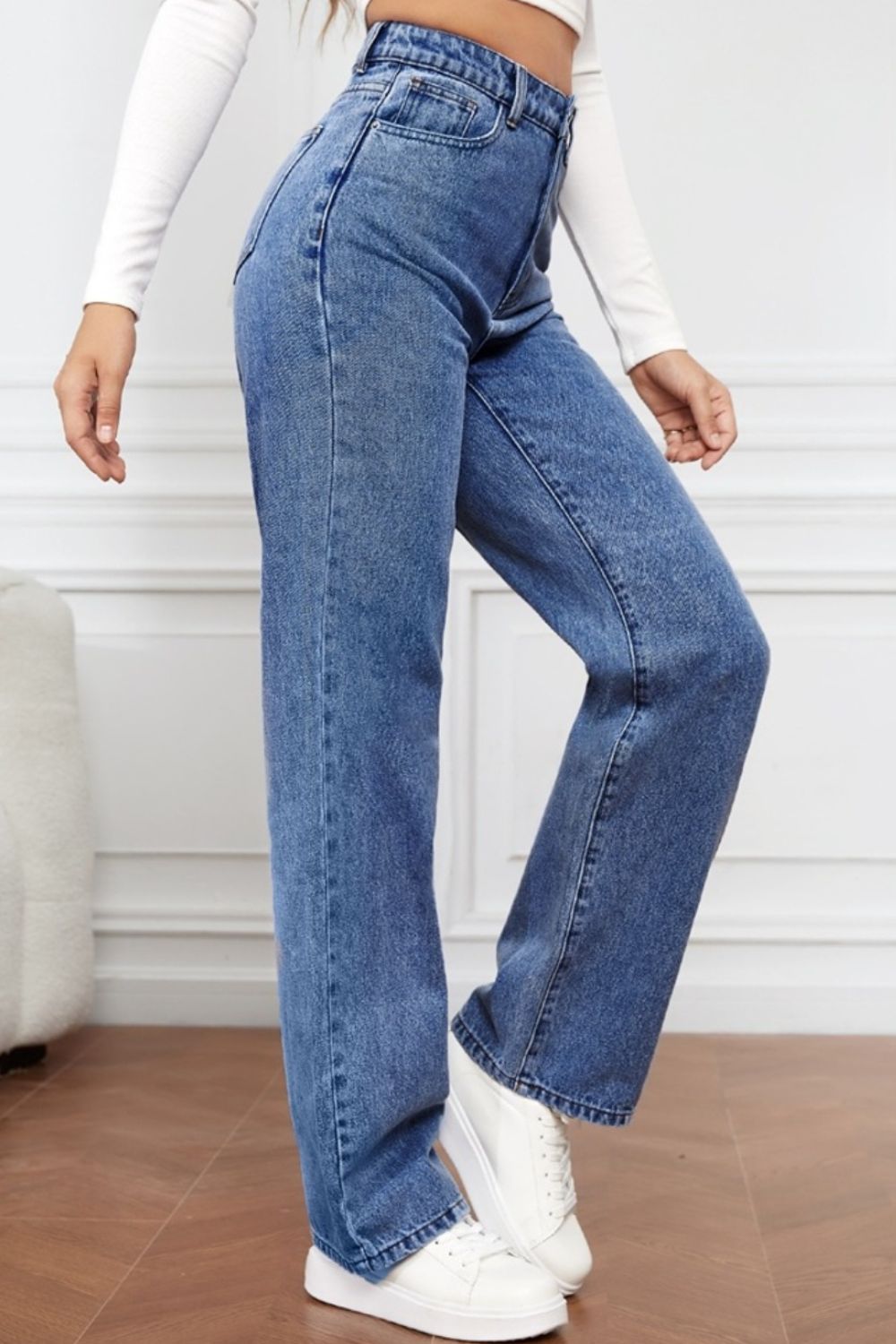 Light blue denim jeans with a wide-leg cut and sculpted waist, styled with white sneakers.