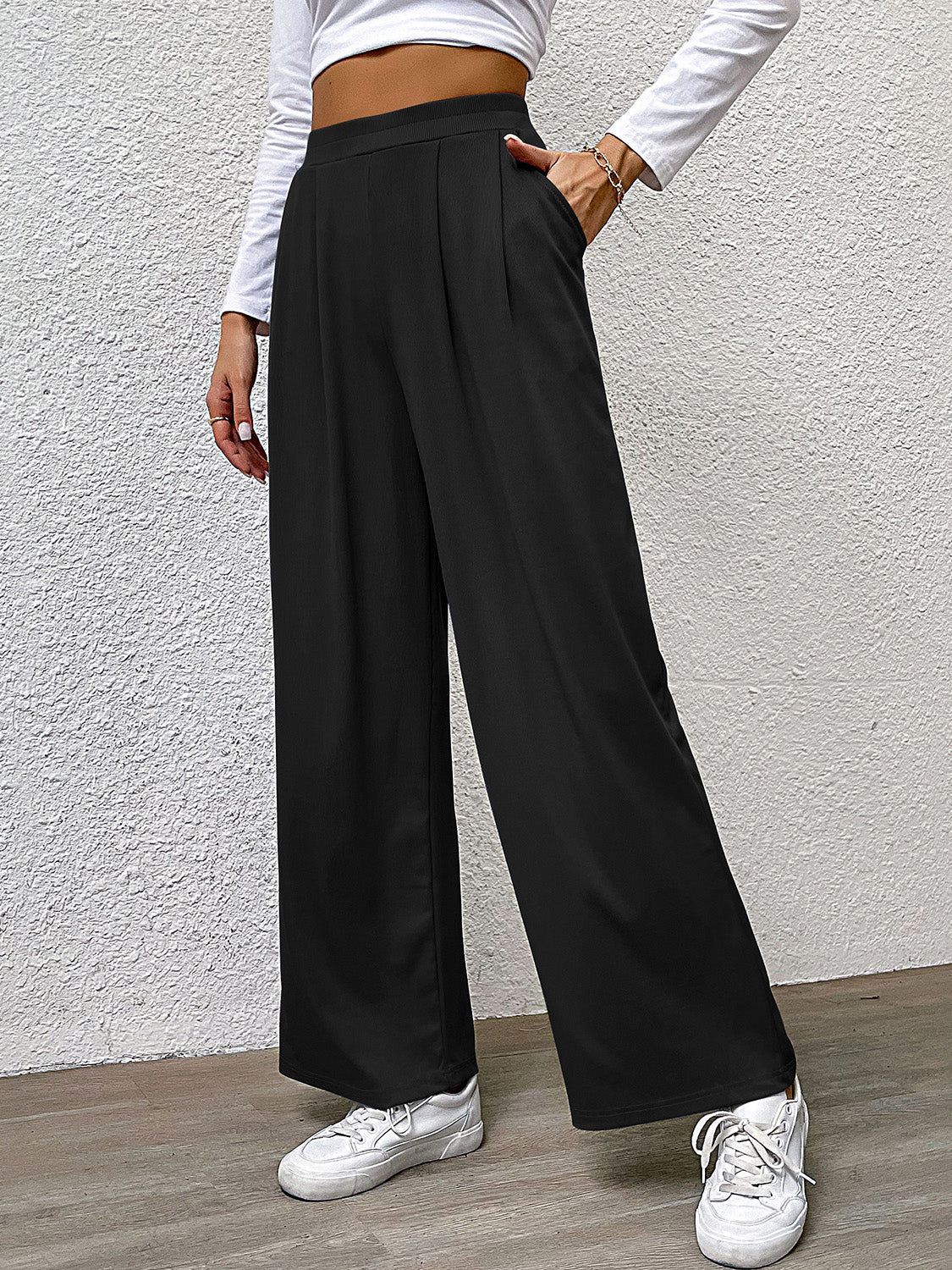 Black wide leg trousers with front pleats and pockets, styled casually.
