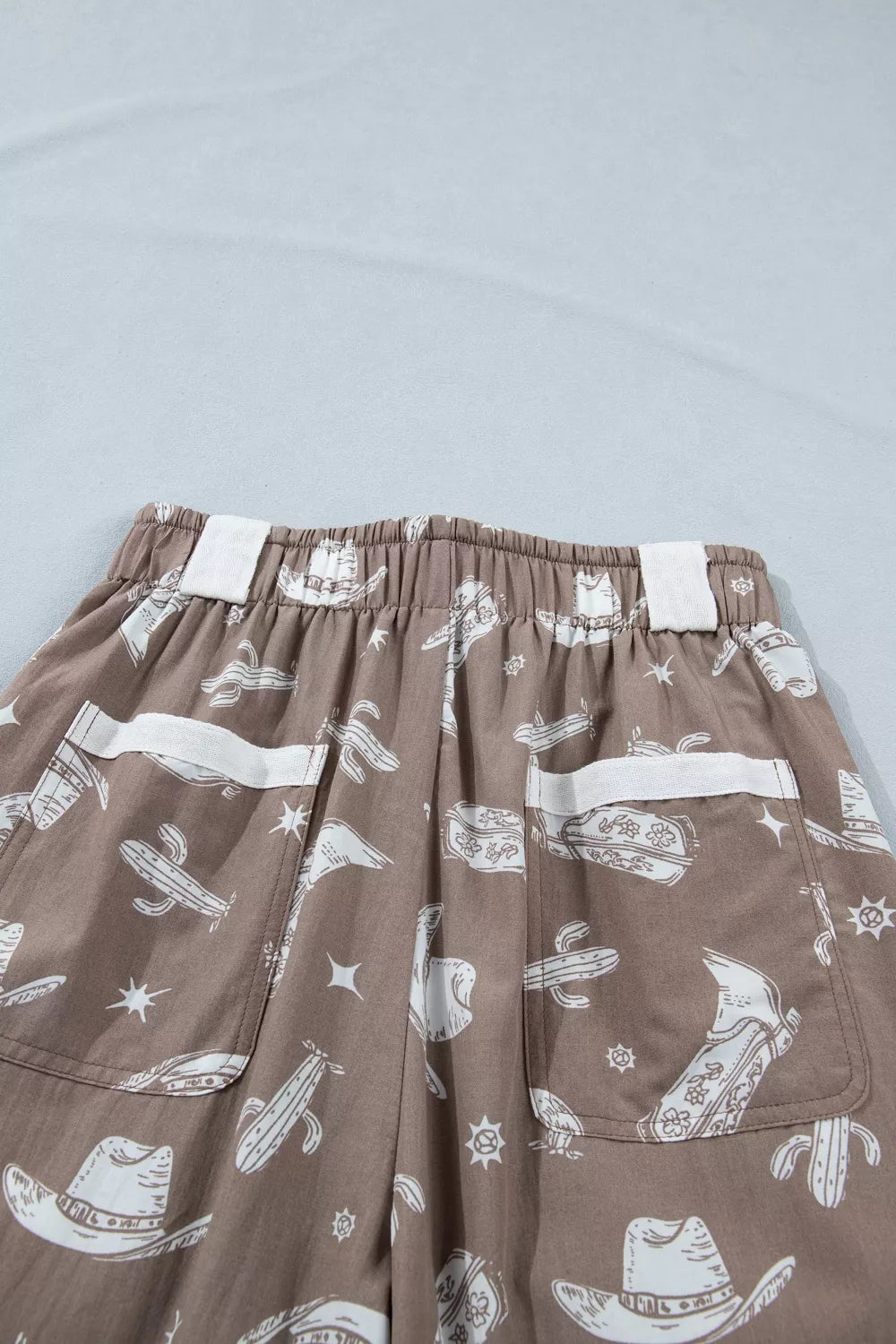 Brown cotton joggers with white western print featuring cactuses and cowboy hats.