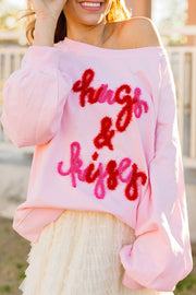 Off-shoulder blush pink sweatshirt with fuzzy red and pink "hugs & kisses" graphic and balloon sleeves.