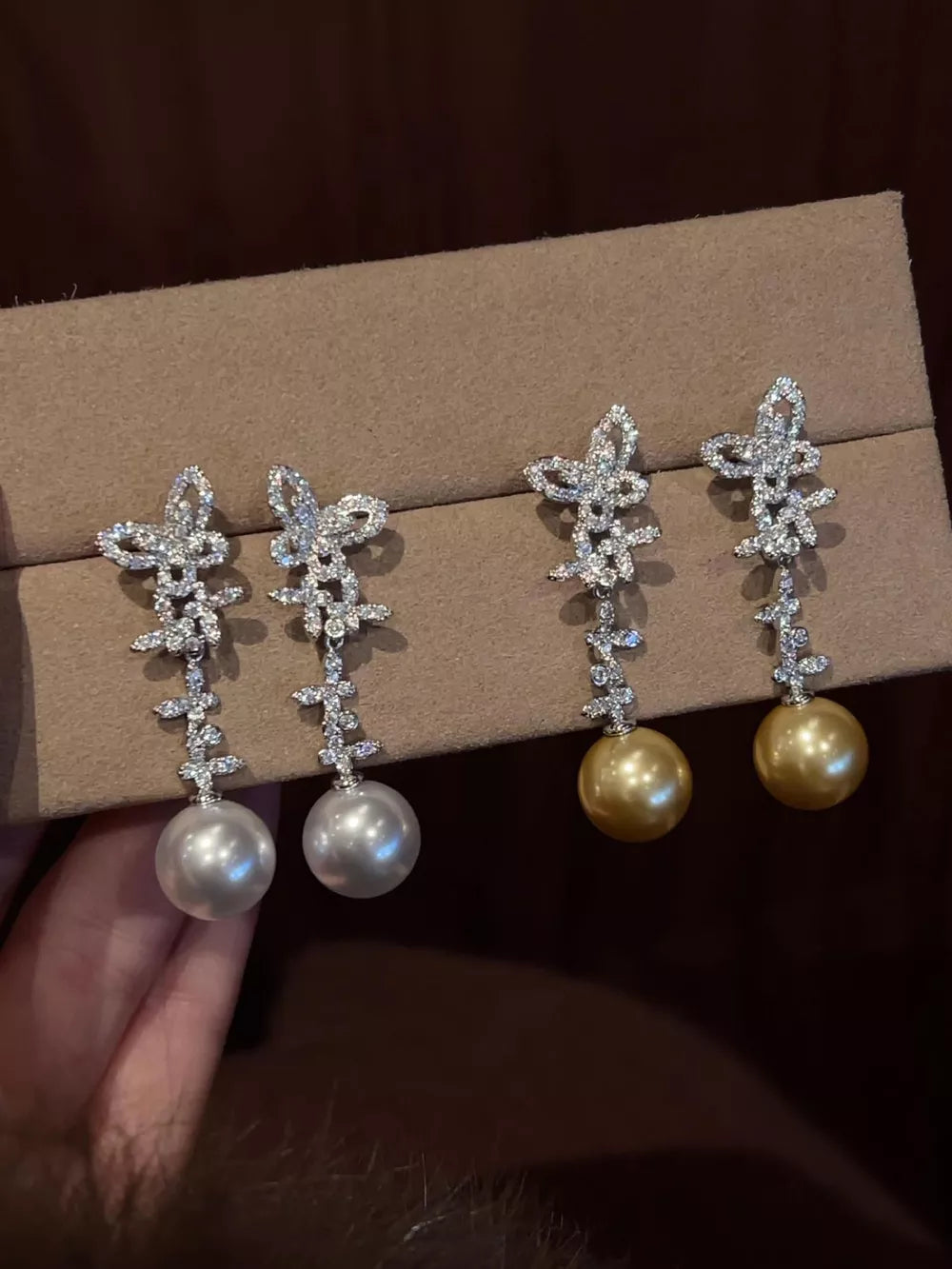 Lustrous butterfly pearl drop earrings in white and pastel yellow with crystal accents.