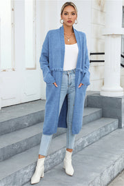 Light blue longline knit cardigan with fringe trim and pockets, worn open over a white top and jeans.