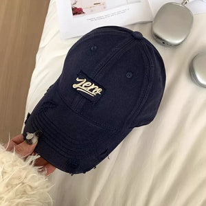 Distressed dark blue cotton baseball cap with embroidered "zero" patch and frayed details.