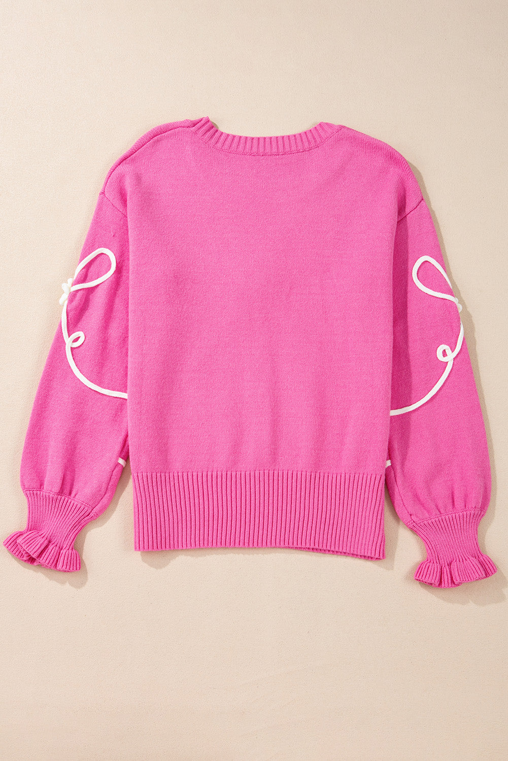 Fuchsia pink knit sweater with white embroidered bow motif on sleeves and ruffled cuffs.