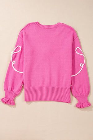 Fuchsia pink knit sweater with white embroidered bow motif on sleeves and ruffled cuffs.