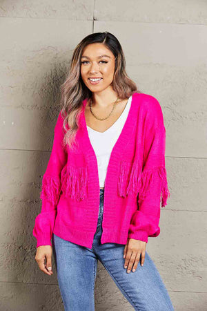 Fuchsia acrylic cardigan with fringe sleeves and a relaxed fit, styled with a white top and jeans.