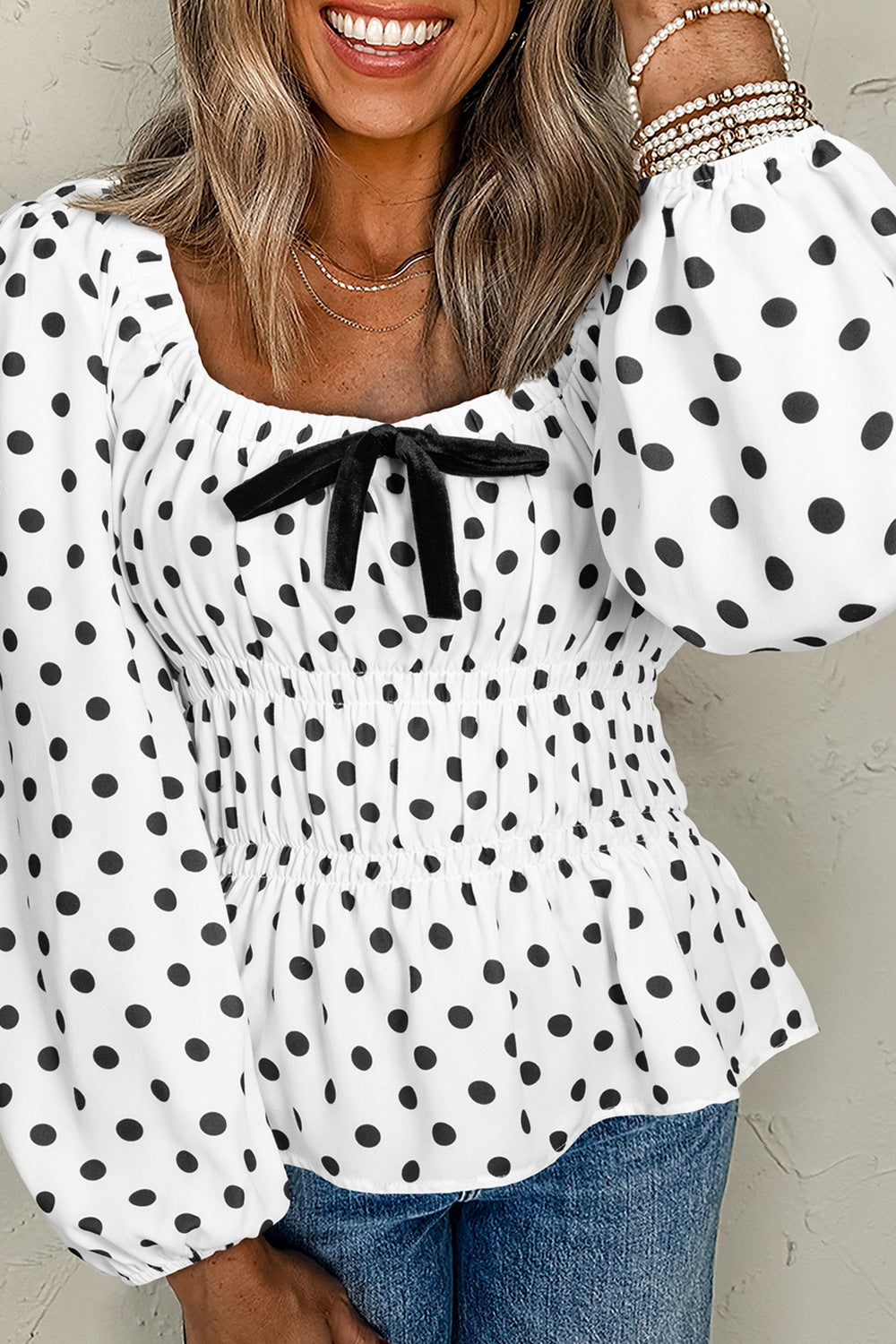 White polka dot blouse with smocked waist, puff sleeves, and black bow detail