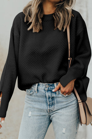 Black textured knit sweater with crew neck and sleeve slits, styled with jeans.