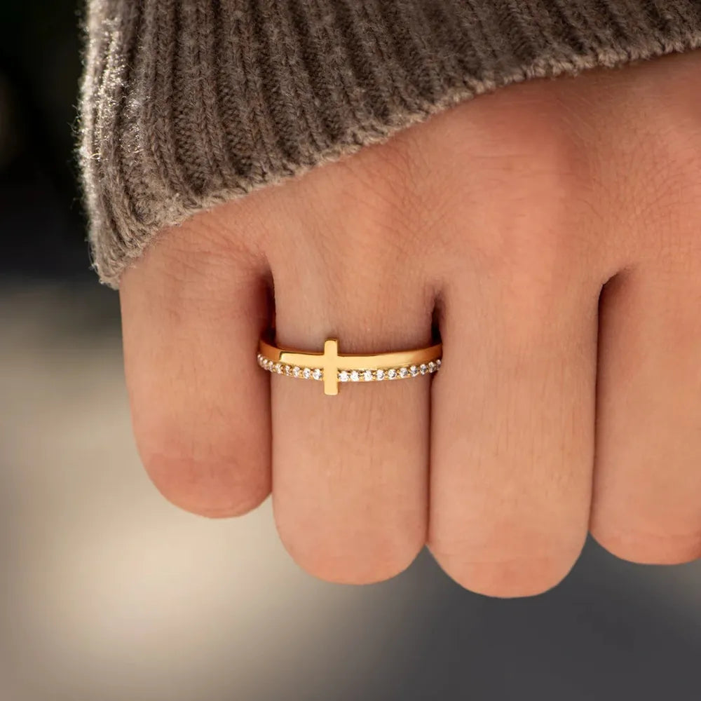 Gold cross ring with diamond trim on a finger