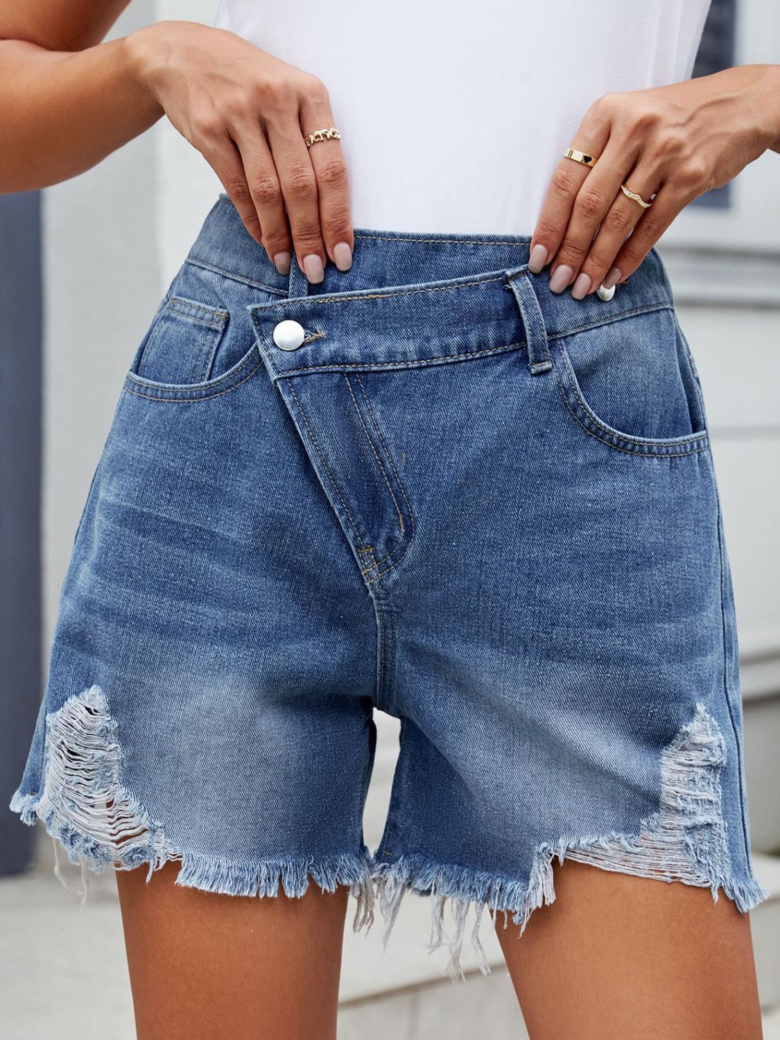 Medium wash denim shorts with asymmetric wrap front, shredded hem and distressed details.