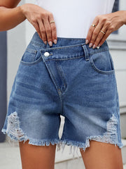 Medium wash denim shorts with asymmetric wrap front, shredded hem and distressed details.