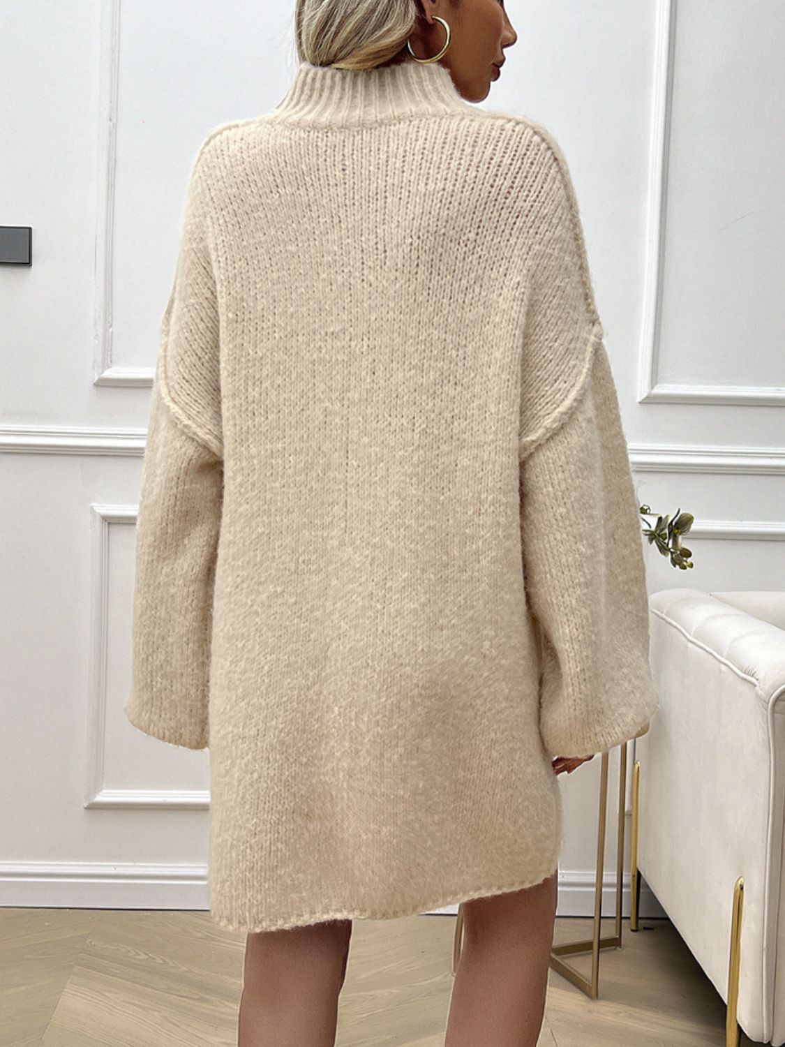 Beige knit mini dress with voluminous sleeves and a high neckline, shown from the back.