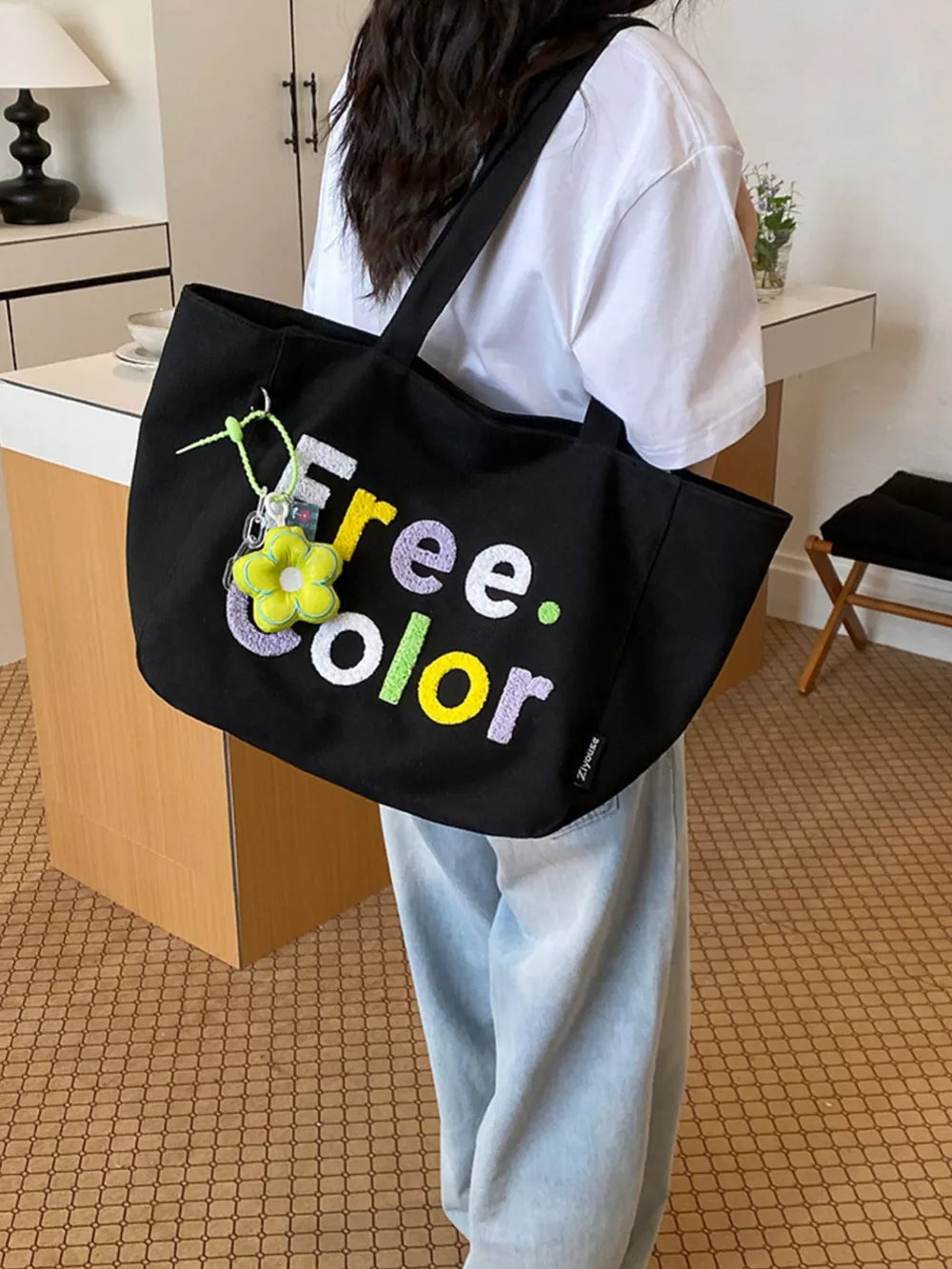 Black canvas shoulder bag with embroidered "Free. Color" text and flower charm