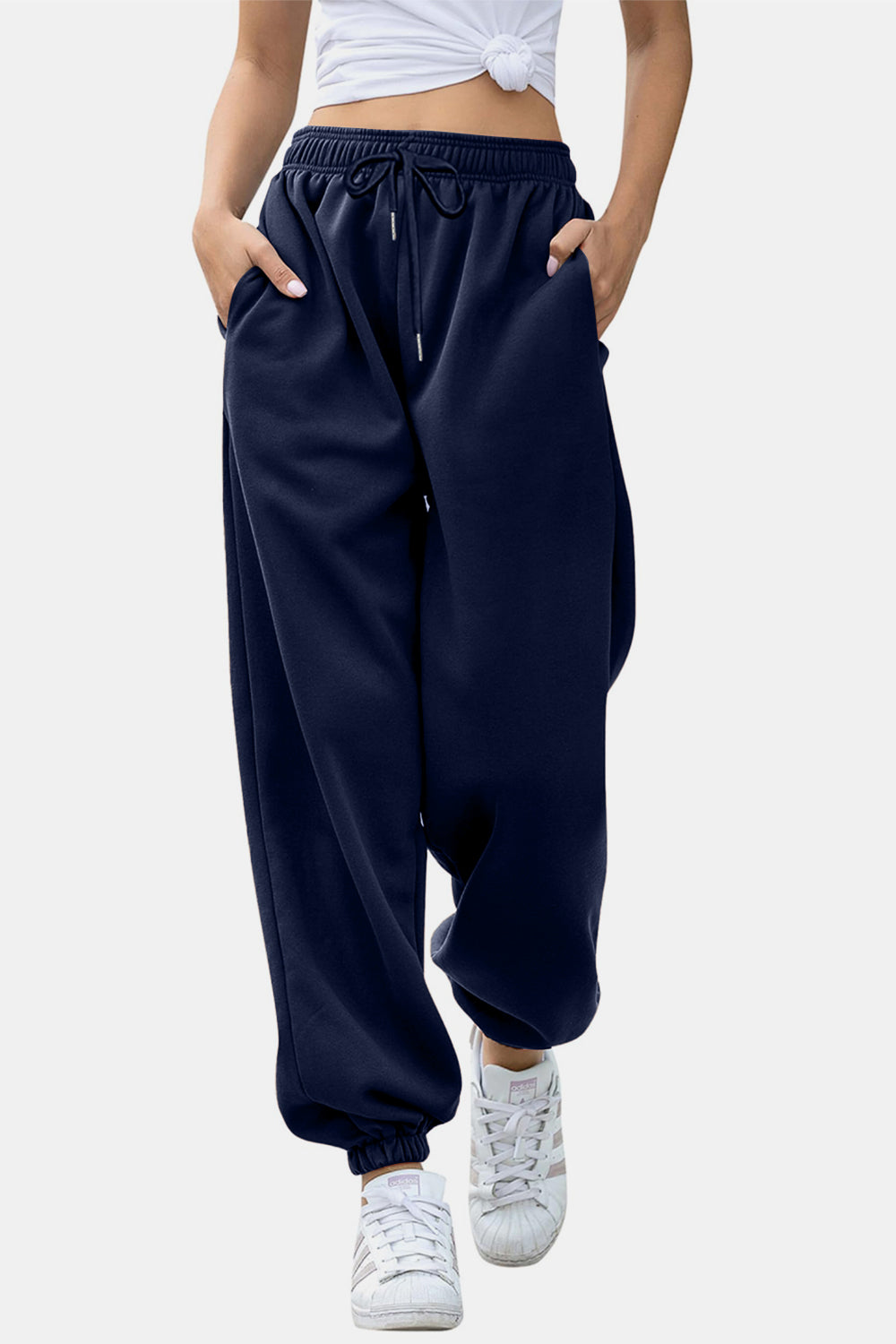Navy sweatpants with gathered cuffs and drawstring waist, styled with white sneakers.